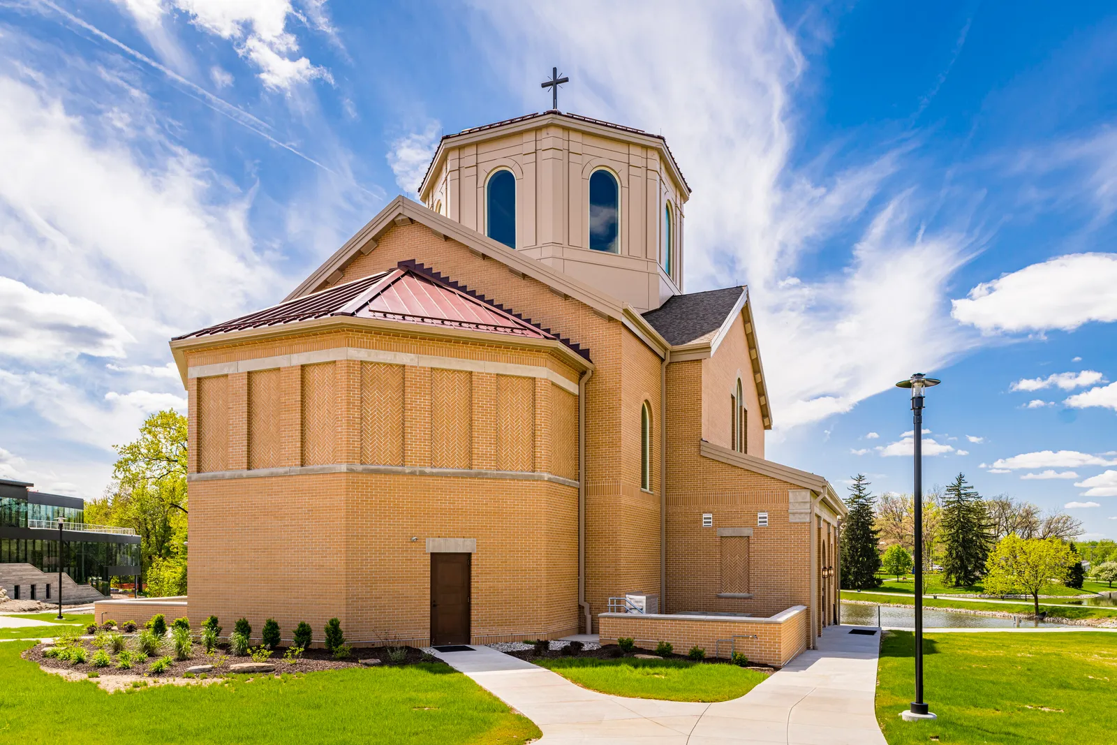 The oratory by day: brick walls with stone trim, the apse and the octagonal lantern tower under a blue sky, campus buildings beyond.