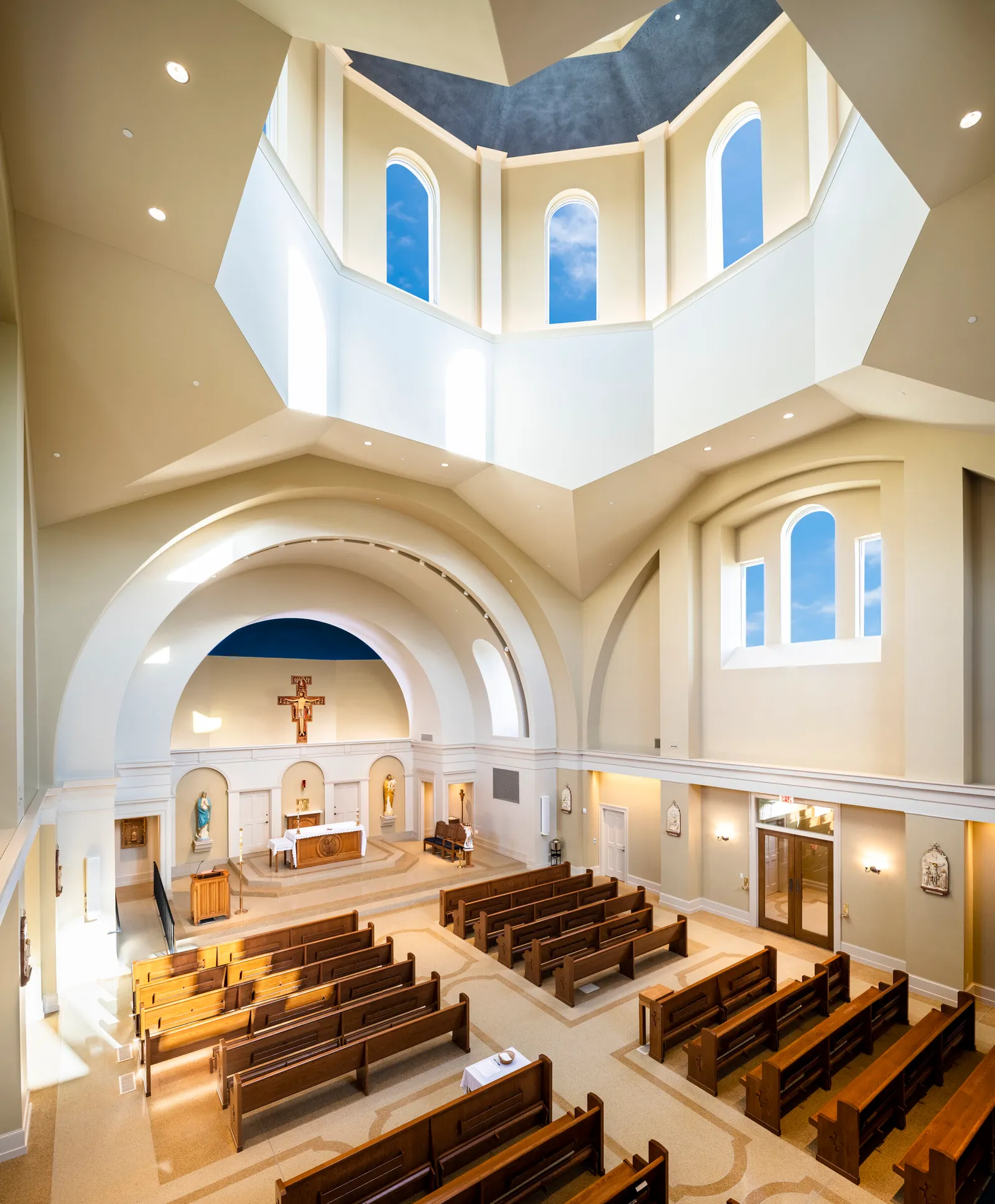 The completed interior looking toward the sanctuary: a tall nave with plain cream walls, light falling from the lantern above the crossing, wooden pews either side of the aisle and the apse beyond.
