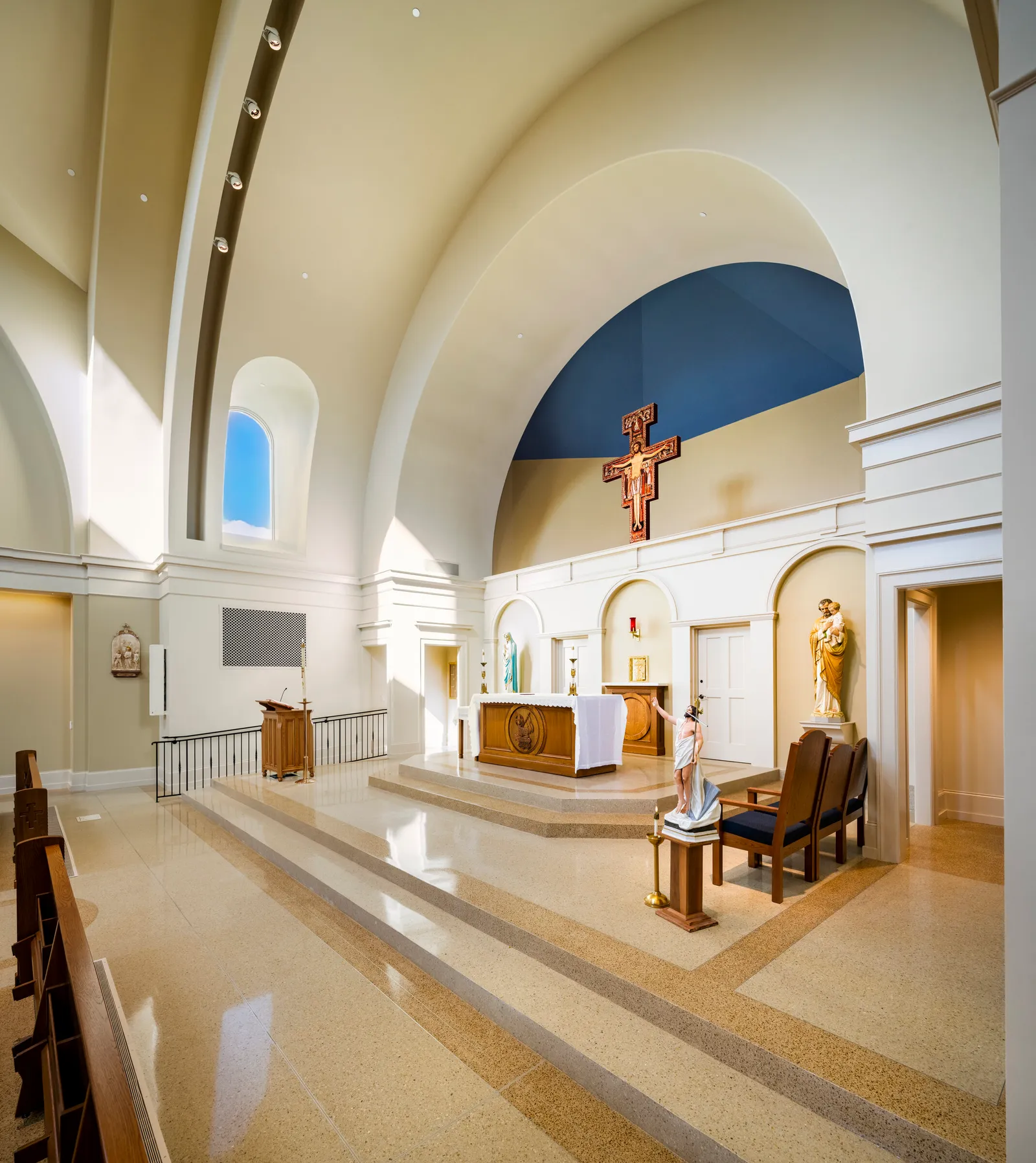 The sanctuary: a rounded apse with a blue-painted half-dome and a painted crucifix above the altar on its raised platform, a side chapel opening at right.