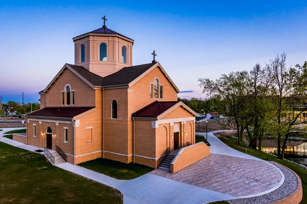 The Oratory of St Francis at dusk, its lantern tower lit from within and reflected in the campus pond