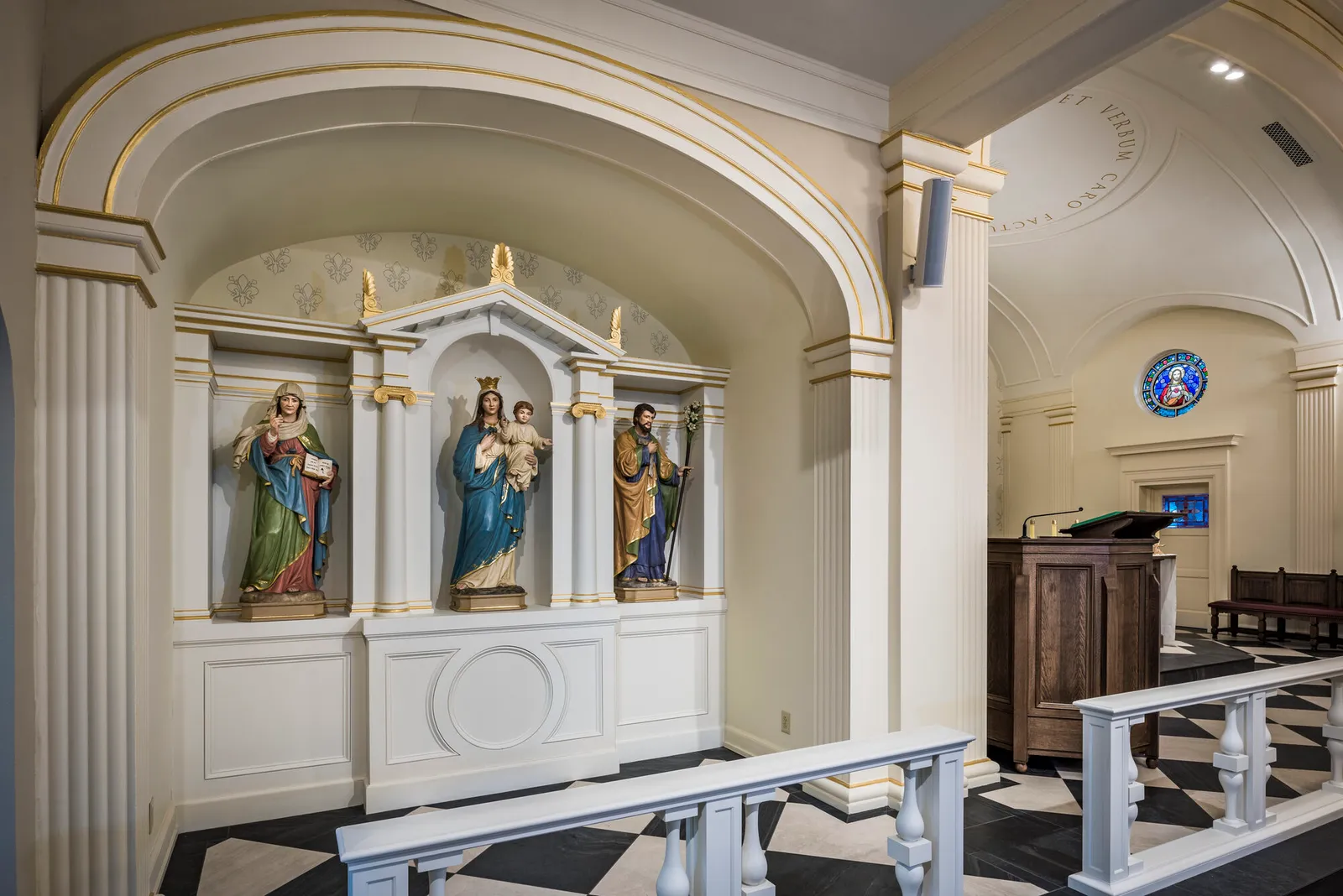 A wall niche with painted statues of the Virgin and Child flanked by two saints, beside a wooden pulpit.