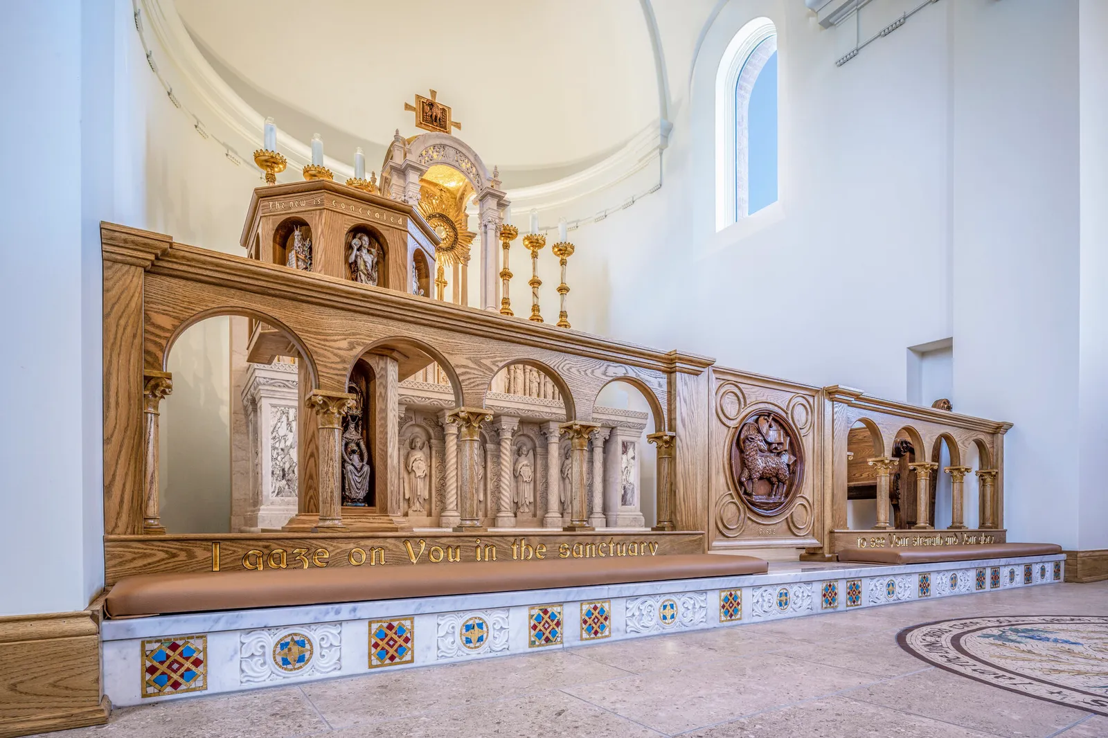 Close view of a carved wood altar rail with a marble arcaded reredos and gilded tabernacle in a chapel sanctuary.