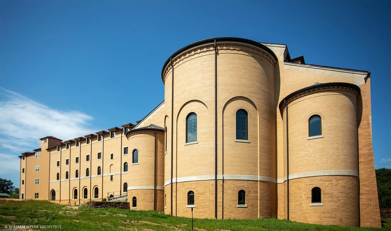The completed apse and east wing in afternoon sun: tiered brick apses with round-arched windows and the long dormitory range beyond.