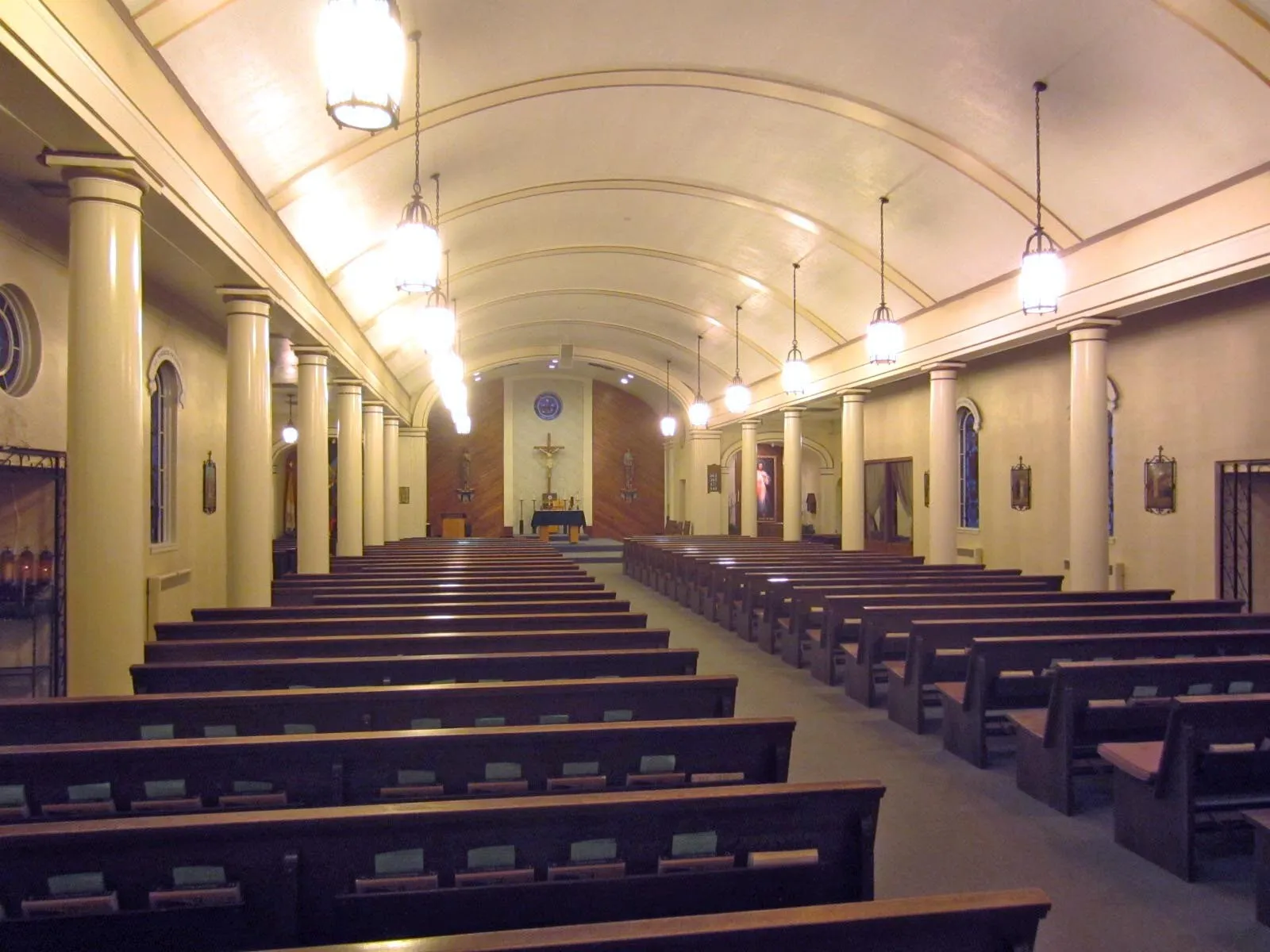 Angled view down the nave before renovation from the rear pews, with columns, hanging lanterns and a carpeted aisle leading toward the sanctuary.