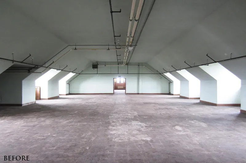The attic space as found: a bare concrete floor under a low sloping ceiling with exposed ducts and pipes, dormer windows along both sides and a single door at the far end.