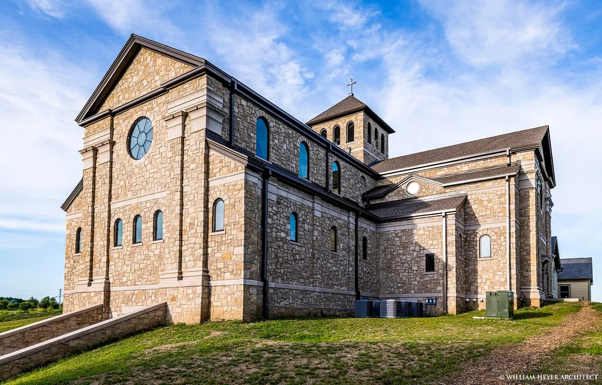 Exterior corner view of the stone abbey church showing the gable end with a rose window and the bell tower topped with a cross.