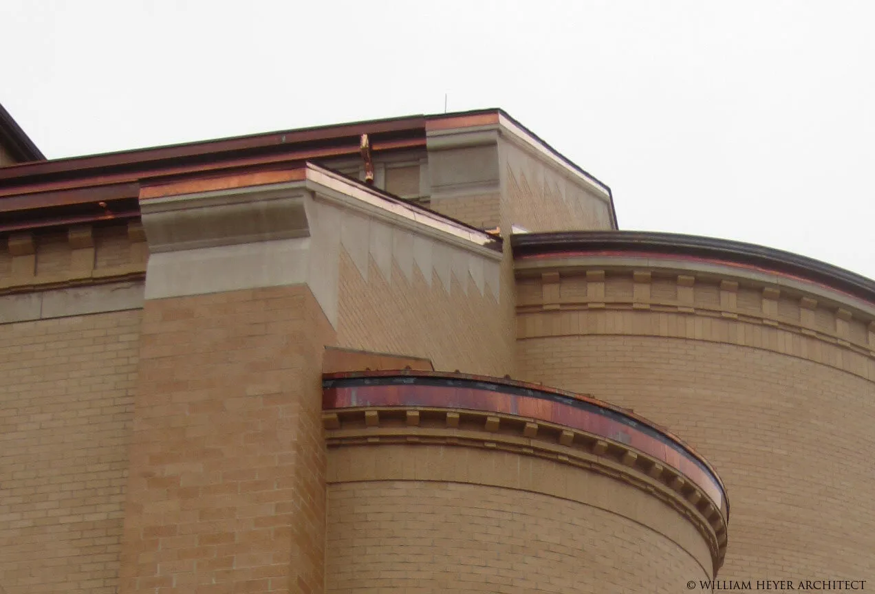 Detail of the exterior: a copper-capped cornice stepping around a curved brick apse beneath an overcast sky.