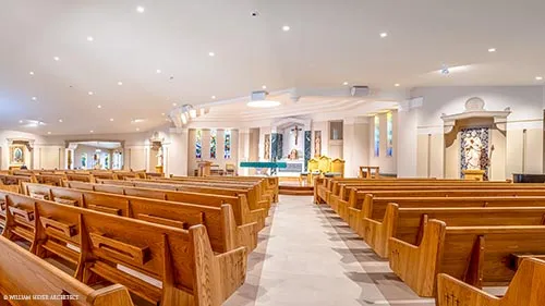 Bright church nave with oak pews on either side of a wide aisle leading to the sanctuary