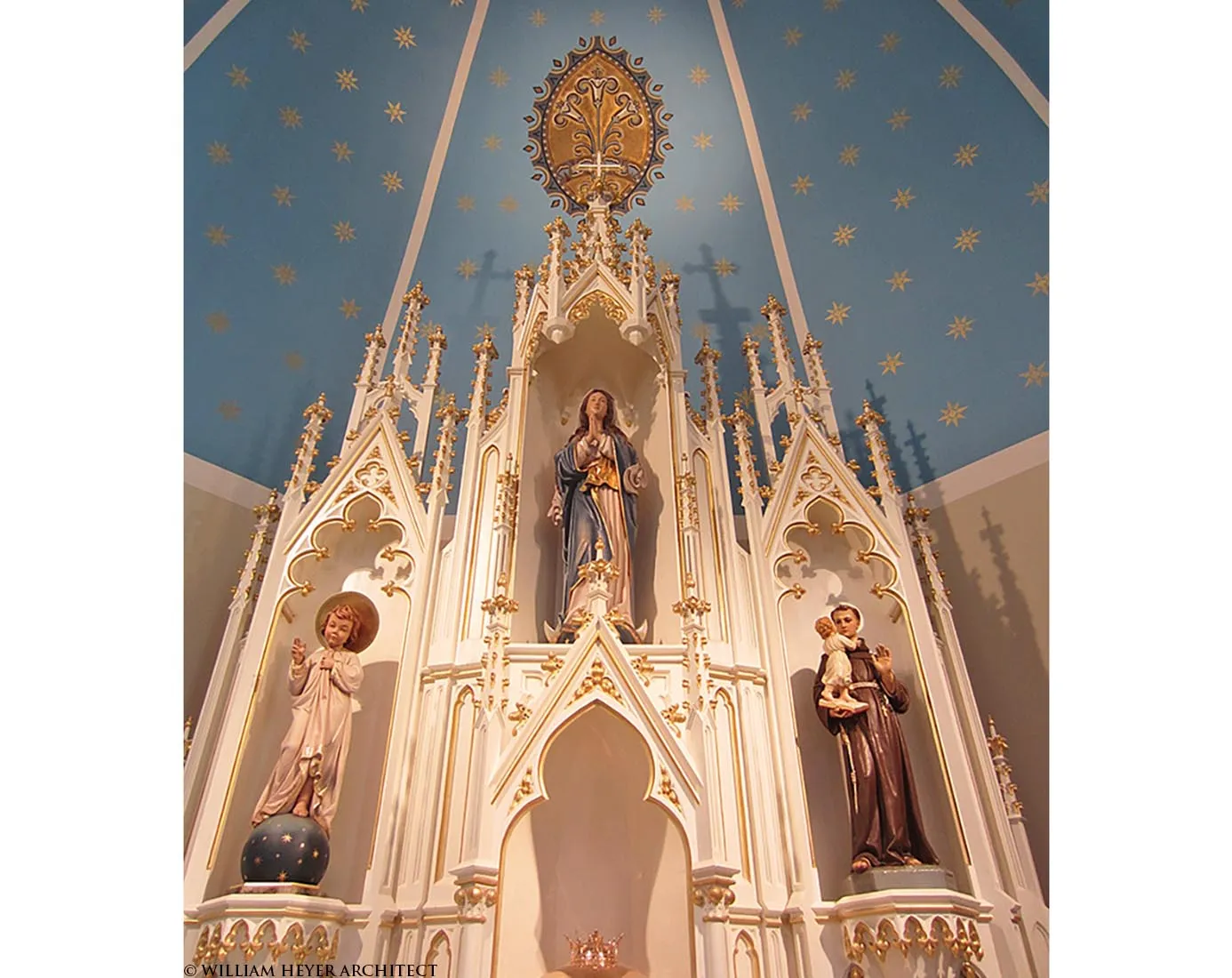 White and gold Gothic reredos with statues of Mary and saints under a star-painted blue ceiling