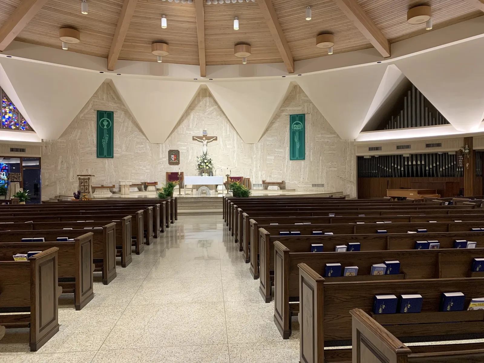 The cathedral nave before renovation: stone walls beneath a folded white ceiling and wood-clad roof, a crucifix above the altar, a speckled stone floor and organ pipes at right.