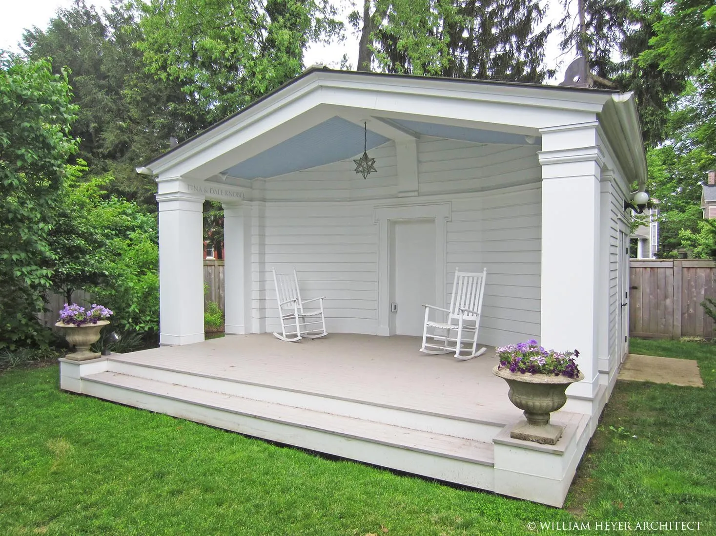 White clapboard garden pavilion with a gabled porch, columns, and two rocking chairs