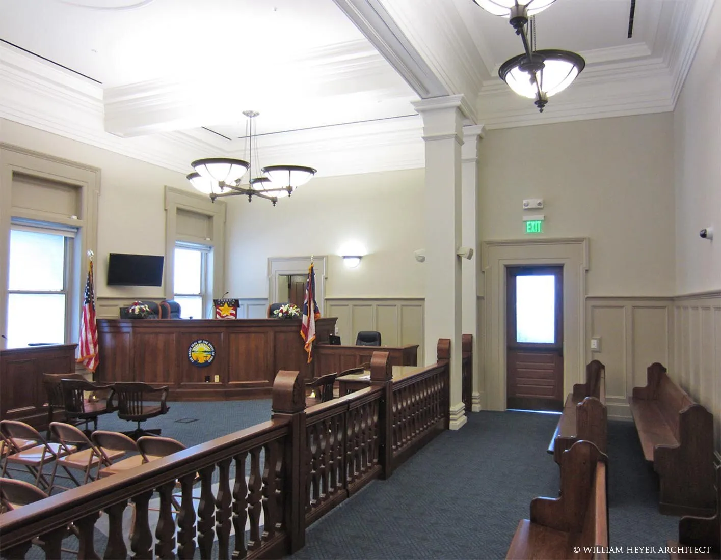 Restored courtroom with judge's bench, wood rail, flags, and coffered ceiling
