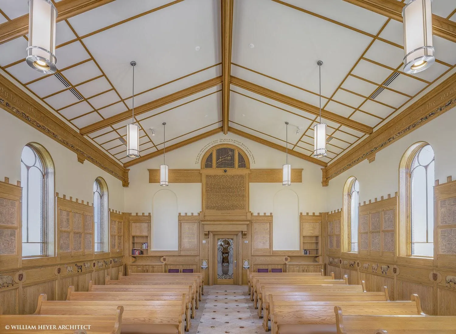 The nave looking toward the rear: oak pews and wainscot beneath the timber roof, and the organ loft under the tower.