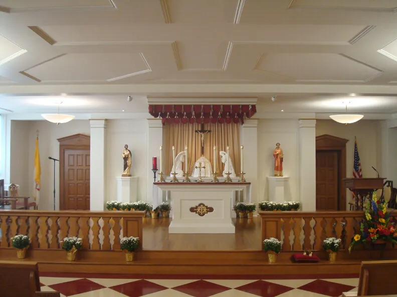 The renovated sanctuary with a coffered ceiling, red valance drapery, a gilded curtain backdrop, a crucifix, and statues flanking the altar.
