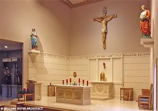 Modern sanctuary with a crucifix above the tabernacle, flanking statues, and an inscribed frieze