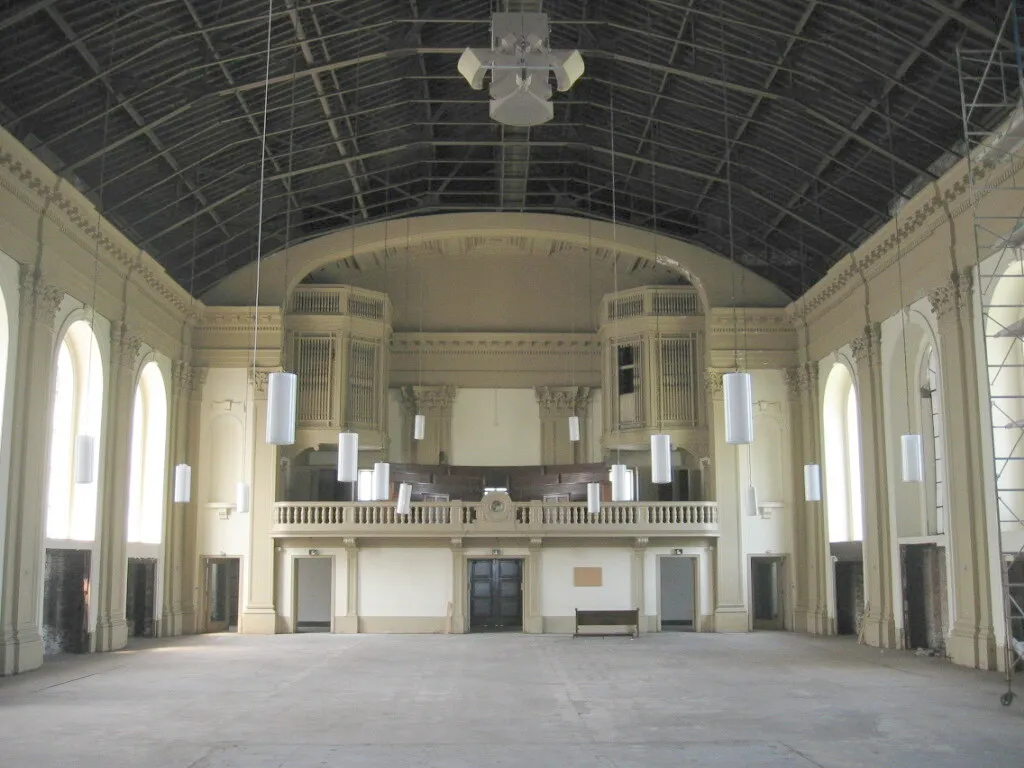 The emptied nave looking toward the choir loft and organ cases before the fire, with the ceiling removed to expose the roof trusses, a bare floor and scaffolding along the right wall.