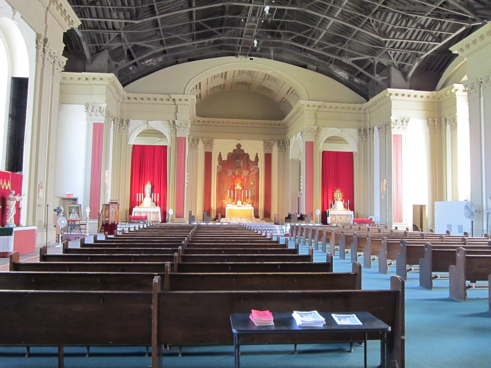 The nave looking toward the sanctuary before the fire, with wood pews, red hangings, the high altar reredos and the roof trusses exposed above the cornice.