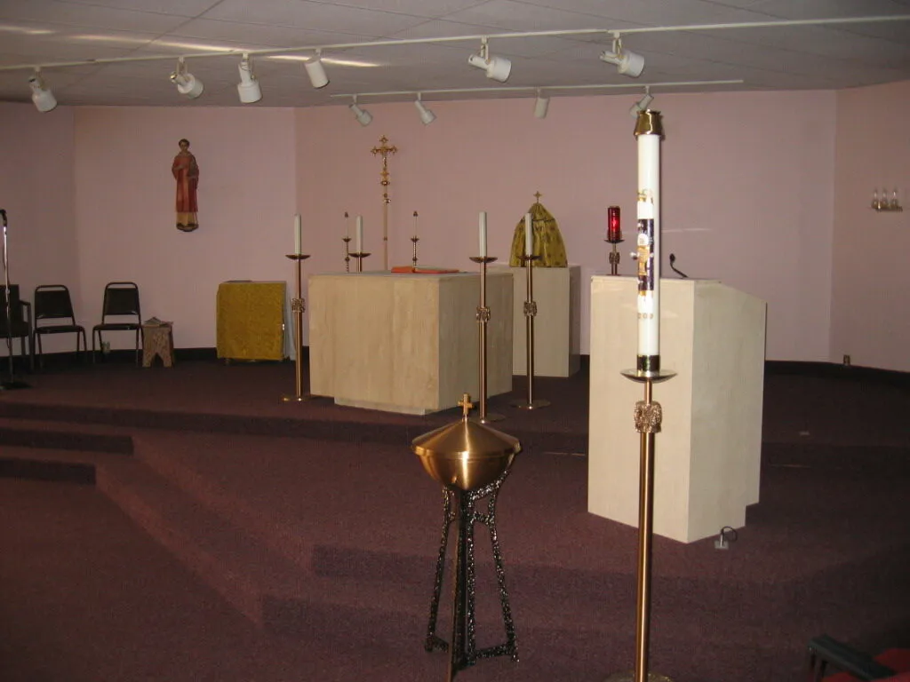 A plain former sanctuary with mauve walls, a drop ceiling with track lighting, and a simple portable altar.