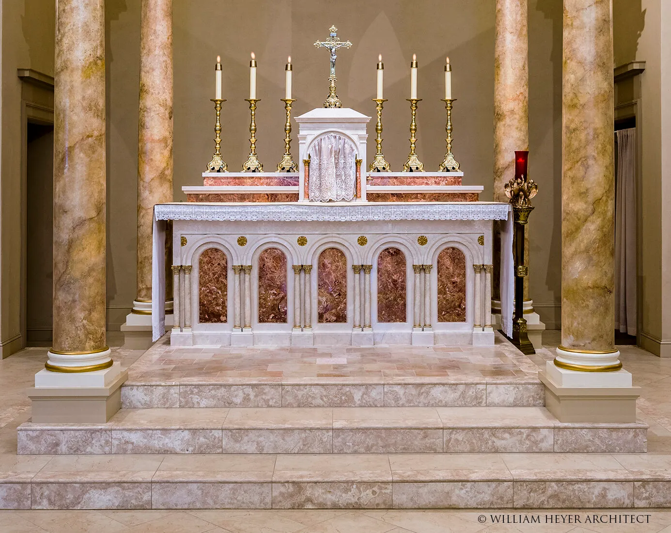 Close view of an altar table with a crucifix and six lit candlesticks flanked by marble columns.