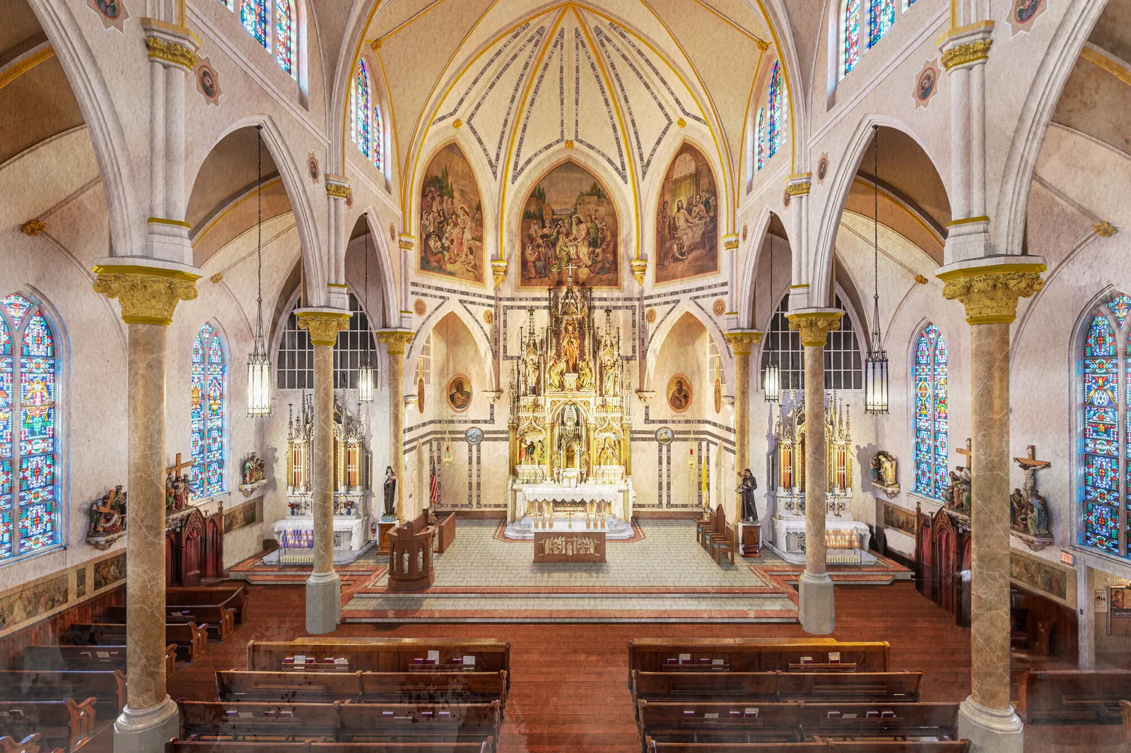 The nave looking toward the sanctuary, with painted Gothic vaulting, murals in the apse, a gilded altarpiece over the high altar, and marble columns with gilded capitals.