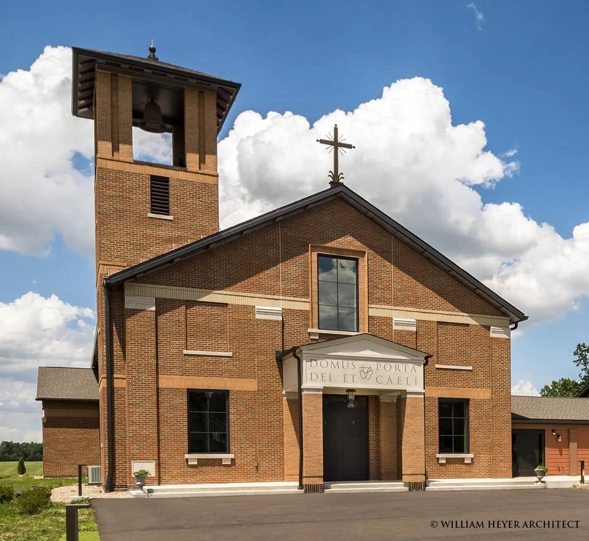 Brick church facade with freestanding bell tower and Latin-inscribed entry pediment
