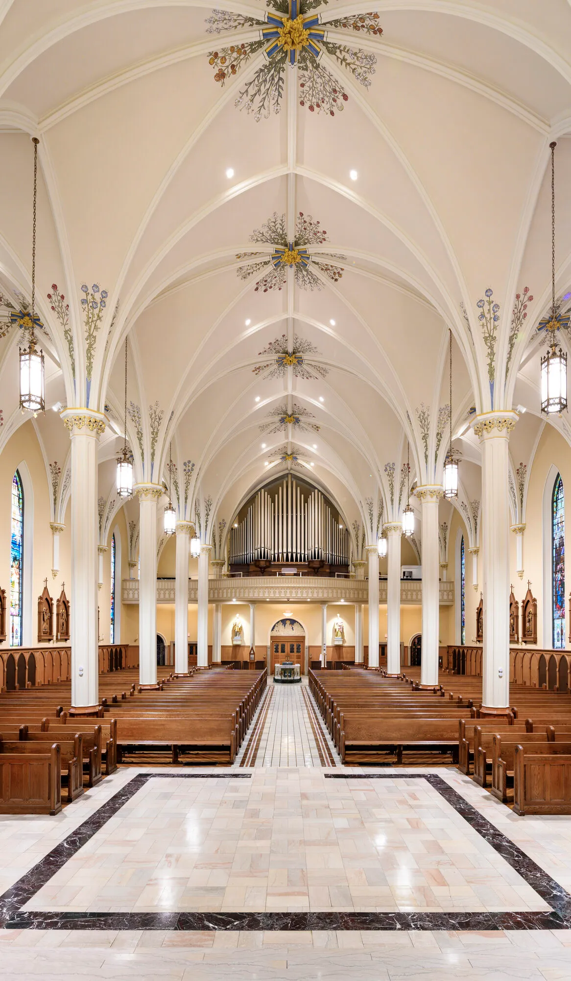 Vertical view from the choir loft down the center aisle of the church, past the organ pipes toward the vaulted nave and pews.