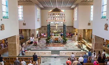 Congregation standing in a wide nave with green marble piers and a canopied altar