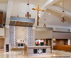 Modern sanctuary with gold crucifix suspended beside a patterned tabernacle tower
