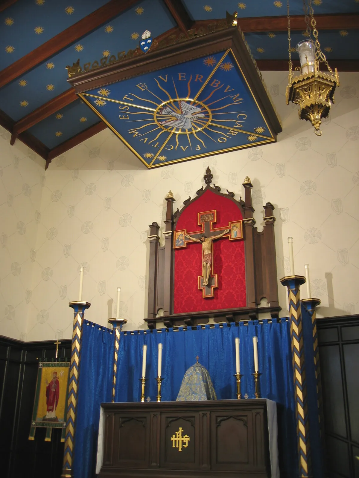 Chapel altar with blue frontal, crucifix reredos, and an inscribed canopy under a starred ceiling