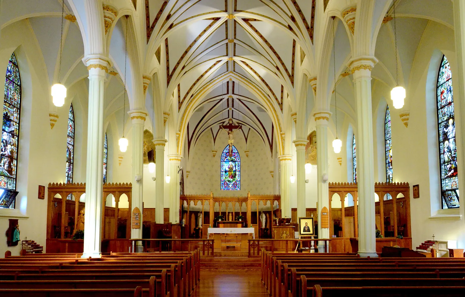 Gothic nave with white vaulted ceiling and stained-glass window above the altar