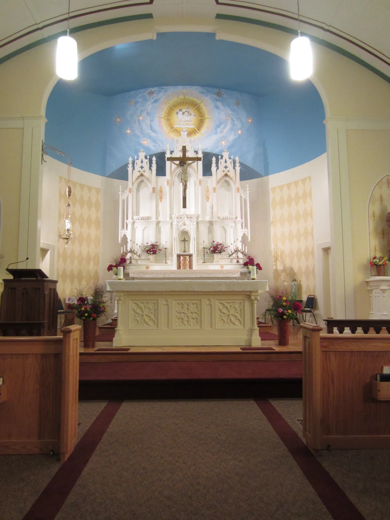 White Gothic altarpiece with crucifix before a painted apse of clouds and radiant dove