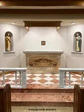 Small chapel with marble altar rail, checkered marble floor, and statues in lit niches