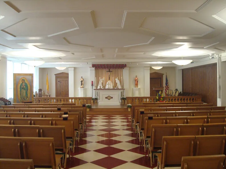 The renovated nave with a red-and-white checkerboard floor, wood pews, an image of Our Lady of Guadalupe, and the sanctuary in the distance.